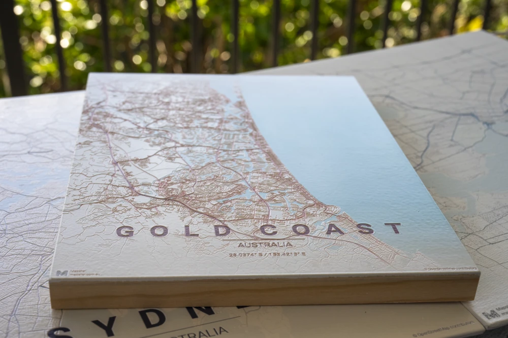 Gold Coast wood-board map stacked on a Sydney print